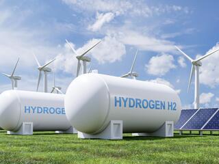 A hydrogen tank in front of solar panels and wind turbines. 