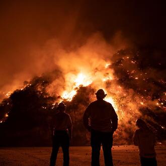 Firefighters fight a large fire burning in the hills.