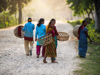 Women carry baskets and wear colorful clothes as they walk down a path