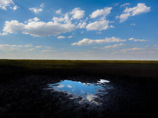 A small bit of water reflects the blue sky and clouds in a mostly dried up fishing pan