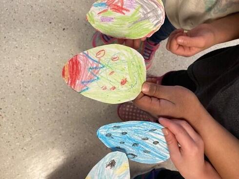 Children hold paper eggs that they decorated in many colors