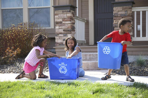 Children place items in recycling bins in front of a house