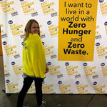 A woman stands in front of a "Zero Hunger | Zero Waste" sign