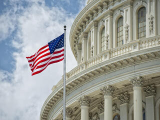 An American flag waves in the wind in front of the Capitol dome