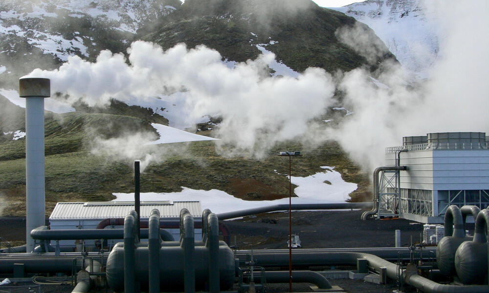 Smoke emits from a pipe at a hydrogen production plant with mountains in the background