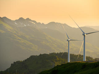 Two wind turbines on a mountain in Alaska with a setting sun and mountains in the background