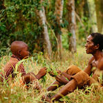 An older man and a younger man sitting in a forest talking