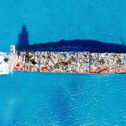 Aerial view of a cargo ship transports containers of garbage across blue waters for recycling factory.