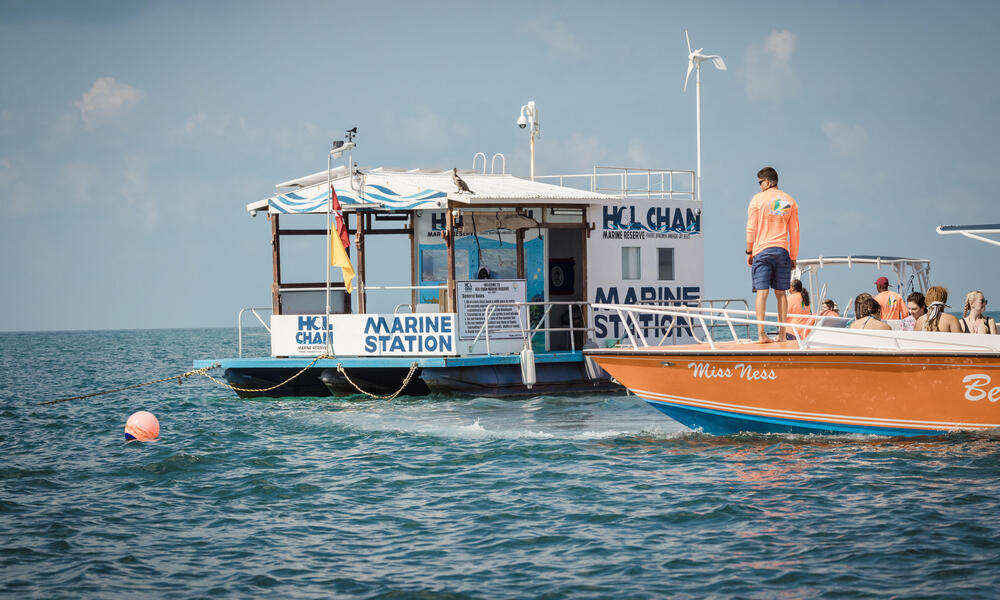 A floating ranger station is approached by an orange boat on a sunny day in Hol Chan, Belize