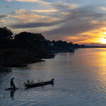 A person stands near a canoe in dwindling light on a river