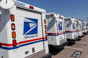 A row of US Postal trucks lined up in a parking lot