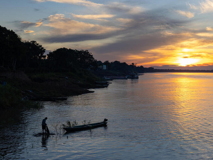 A person stands near a canoe in dwindling light on a river