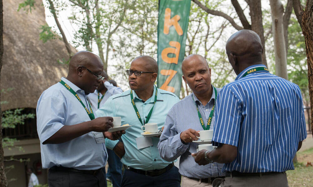 Four men outdoors holding coffee and chatting